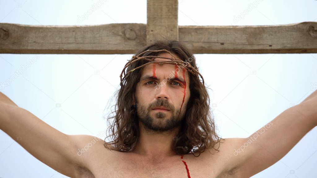 Exhausted Jesus nailed to cross, looking into camera, atoning humanity sins