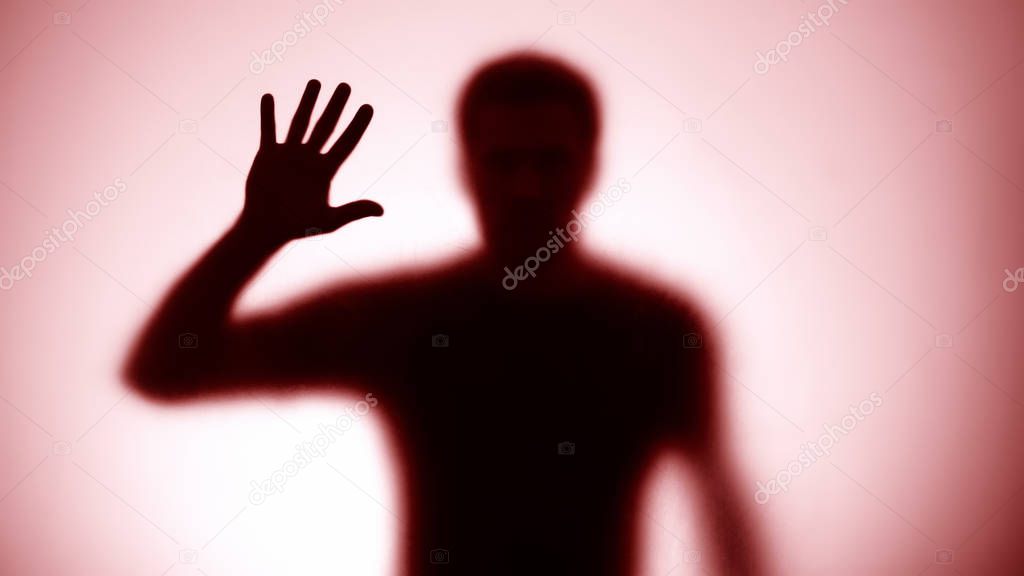 Male silhouette looking through glass wall, red light background, war alarm