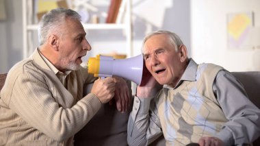 Senior man shouting bullhorn to deaf friend, old aged health, deafness treatment clipart