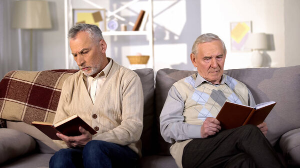 Senior men reading books in nursing home sitting sofa, retirement leisure, hobby