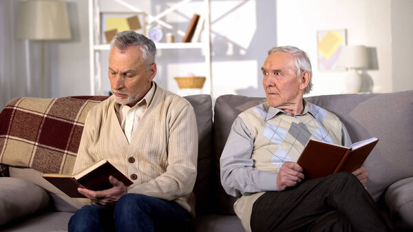 Displeased old man looking at offended friend reading book, relations conflict