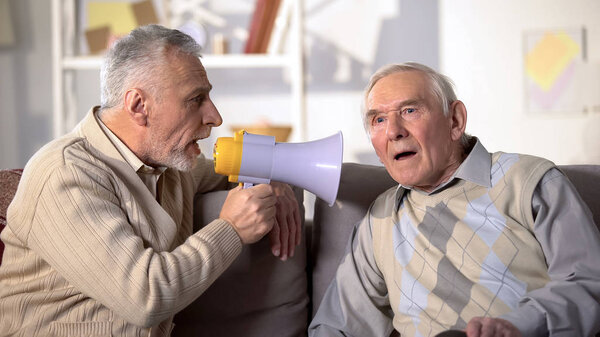 Elderly male talking in megaphone to deaf old friend, health problems, close-up