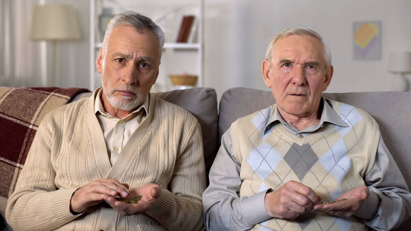 Elderly men counting coins and looking camera, low social payment, poverty