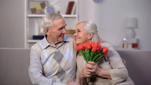 Feliz Anciana Sosteniendo Tulipanes Rojos Mirando Con Amor Marido Mayor —  Fotos de Stock