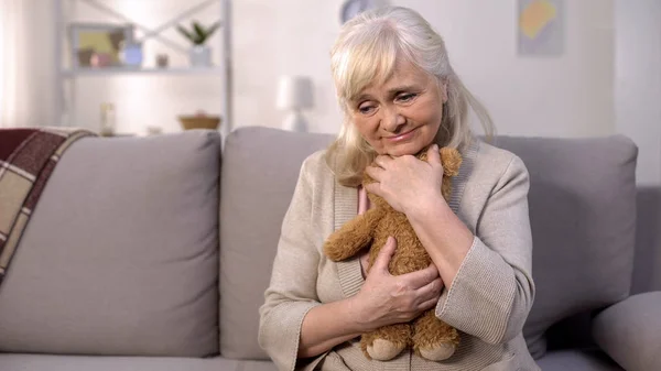 Sad old woman hugging teddy bear boy missing grandchildren, long separation