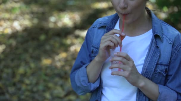 Mujer joven descuidada bebiendo agua de soda tirando paja de plástico en el parque, basura — Vídeo de stock