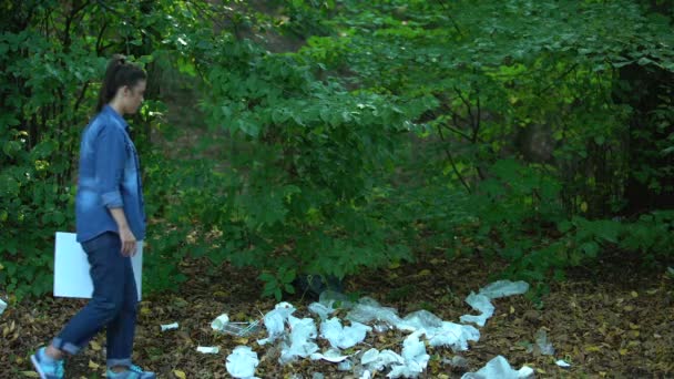 Besorgte Frau hält Schild mit dem rettenden Planeten zu Fuß Wald Mülldeponie, Plastikmüll — Stockvideo