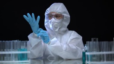 Laboratuvar asistanı koruyucu giysi giyiyor ve virüs ile test tüpleri üzerinde çalışıyor.