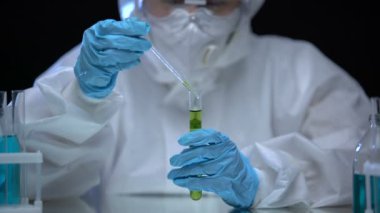 Koruyucu kıyafetli bilim adamı test tüpünden radyasyonlu sıvı örneği alıyor.