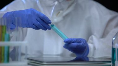 Zehirli laboratuvar çalışanı zararlı sıvıyı inceliyor ve tablet ve deney üzerine notlar alıyor.