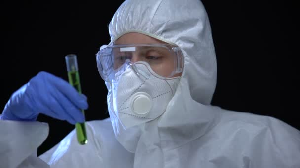 Vrouw in beschermende pak onderzoekt groene vloeistof ioniserende straling, illegaal lab — Stockvideo