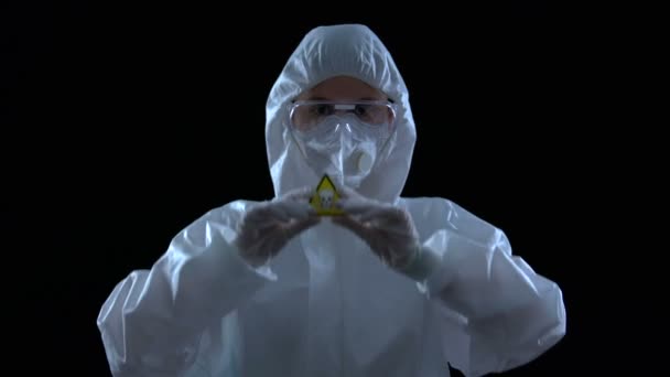 Ученый в защитном костюме держит в руках символ яда, черный фон — стоковое видео