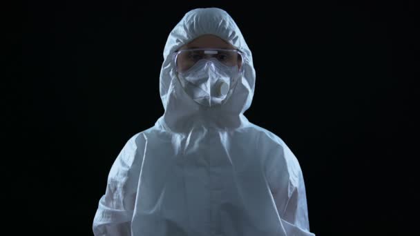 Ученый в защитном костюме и маске смотрит на камеру на черном фоне — стоковое видео