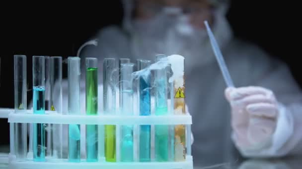 Un scientifique dépose un échantillon à ébullition liquide dans une éprouvette avec un symbole d'avertissement — Video