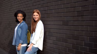 İki gülümseyen üniversite öğrencileri tuğla duvar, boş zaman üniversite kampüsü eğilerek