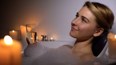 Köpük köpükler ve mumlar ile banyoda yatan, şampanya içen rüya gibi bir kadın