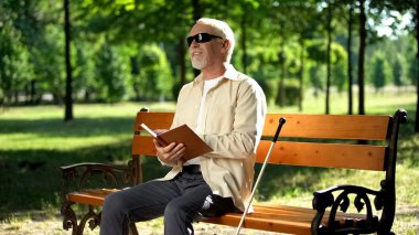 Mutlu kör emekli braille kitapta komik hikaye okuma, parkta dinlenme zevk