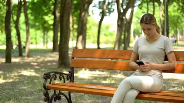 Parkta bankta oturan akıllı telefonu kullanan, sosyal medyada boş zaman ları kaydıran bayan