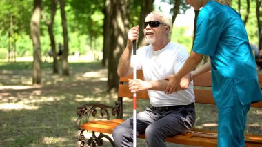 Üniformalı hemşire yaşlı kör adam ayağa kalkmak için yardım, yardım ve bakım