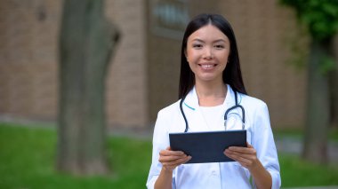 Hastane parkında tablet Pc üzerinde çalışan Gülümseyen kadın doktor, tıbbi araştırma