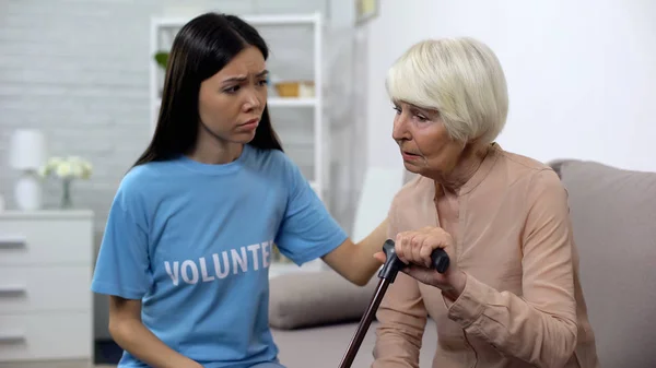 Caring social activist comforting sad elderly woman with walking stick, support