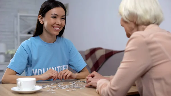 老人ホームでパズルゲームをする老婦人を助ける若いボランティア — ストック写真