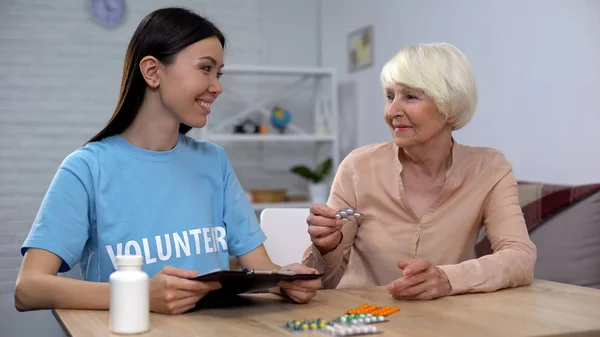 Female volunteer giving free medicines to aged lady, social insurance, help