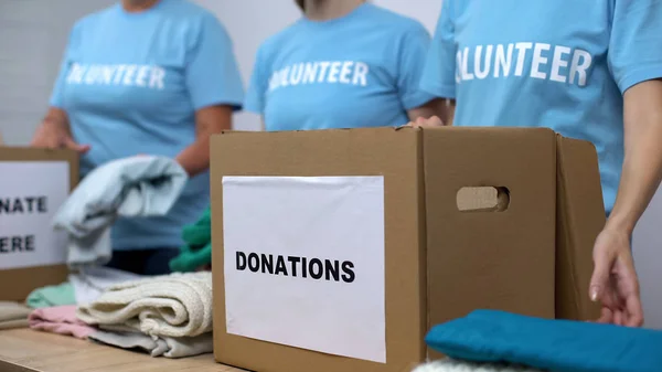 Social center volunteers putting clothes in donation boxes, altruism generosity