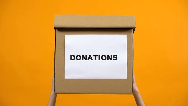 Χέρια Που Κρατούν Κουτί Δωρεών Πορτοκαλί Φόντο Ανθρωπιστική Βοήθεια Αλτρουισμός — Φωτογραφία Αρχείου