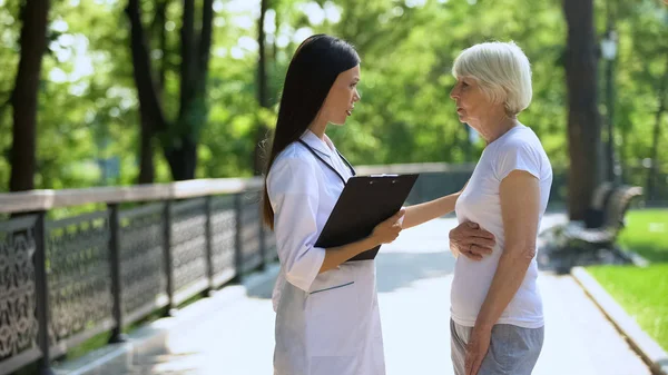 Oude Vrouw Klagen Buikpijn Aan Jonge Verpleegster Ziekenhuis Park Gezondheidszorg — Stockfoto