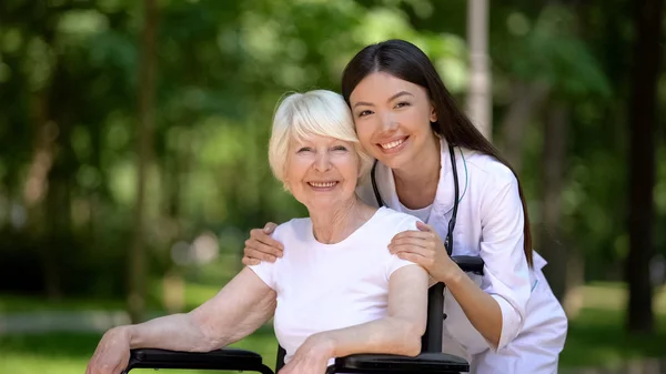 Uśmiechnięta Kobieta Pielęgniarka Przytulanie Niepełnosprawnych Starszych Kobiet Patrząc Kamerę — Zdjęcie stockowe