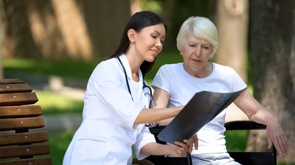 Enfermera Sonriente Mostrando Radiografía Columna Anciana Silla Ruedas Parque Recuperación —  Fotos de Stock