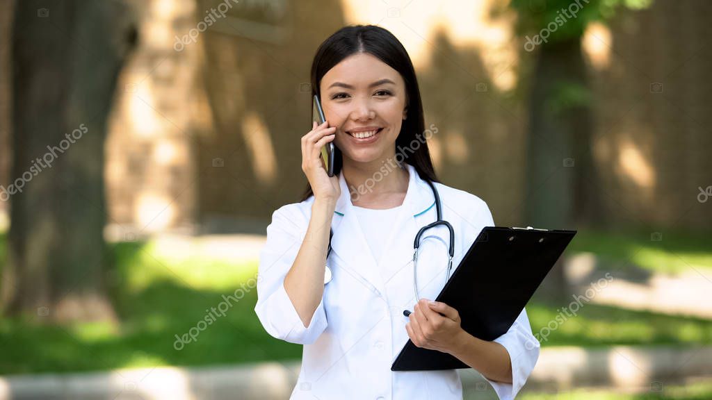 Beautiful nurse talking smartphone with patient at rehabilitation center park