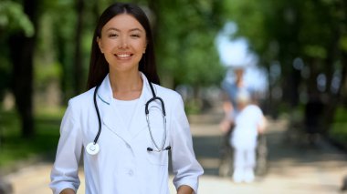 Rehabilitasyon merkezi parkta kameraya gülümseyen mutlu doktor, sağlık kliniği reklam