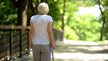 Rehabilitasyon merkezi parkında yürüyüş çerçevesi ile hareket eden yaşlı kadın, arka görüş