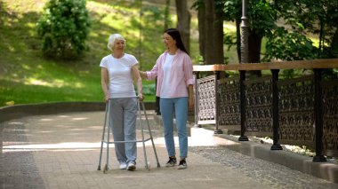 Granddaughter supporting disabled grandma with walking frame, day in park clipart