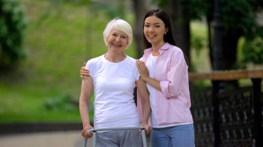 Grandmother with walking frame and young female hugging and smiling at camera clipart