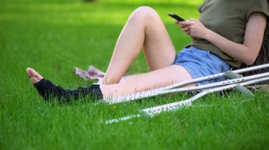Koltuk değnekleri akıllı telefon kaydırma ile ayak bileği parantez oturma parkı kadın, kırık