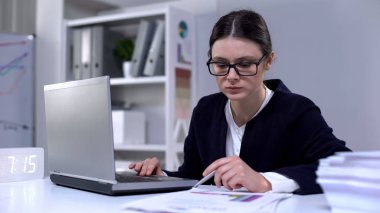 Kadın ofis çalışanı dizüstü bilgisayar ve belgelerdeki bilgilere bakarak, iş