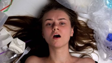 Çöpler arasında yatan plastik çöplerle kaplı bayan, ekolojik felaket