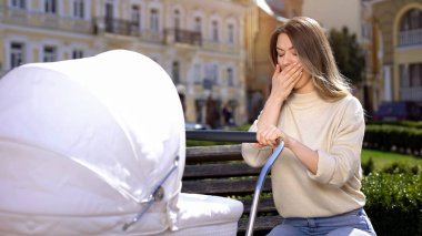 Park bankında oturan bebek arabası sallanan esneyen anne, uykusuzluk
