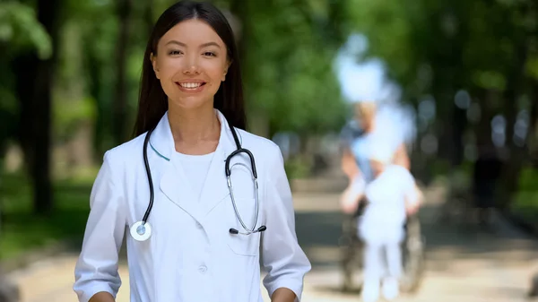 Uśmiechnięty Kobieta Lekarz Patrząc Aparacie Parku Pobliżu Centrum Rehabilitacji — Zdjęcie stockowe