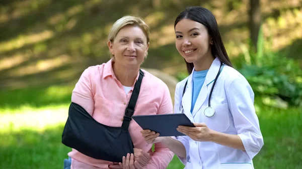 Médico Pediátrico Com Comprimido Mulher Idosa Estilingue Braço Sorrindo Câmera — Fotografia de Stock