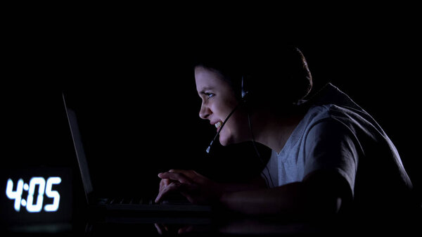 Женщина-геймер в наушниках, играющая в видеоигры поздно ночью, компьютерная зависимость
