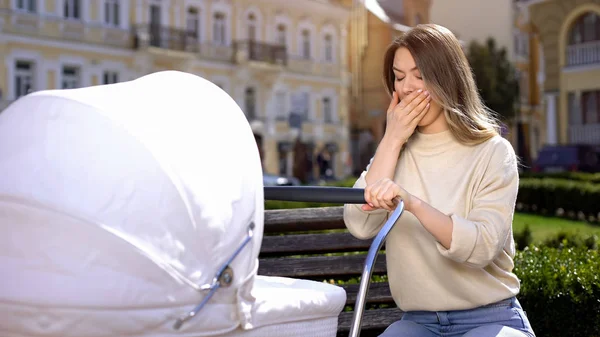 Park bankında oturan bebek arabası sallanan esneyen anne, uykusuzluk