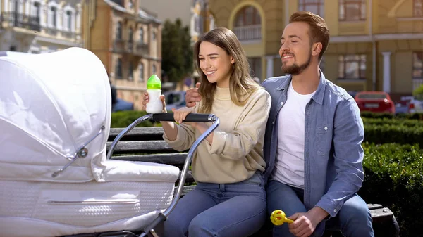 Alegres Padres Leche Biberón Sentado Banco Del Parque Mirando Bebé — Foto de Stock