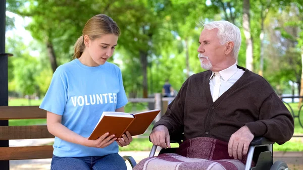Jovem Voluntária Leitura Livro Para Pensionista Deficiente Cadeira Rodas Cuidados — Fotografia de Stock