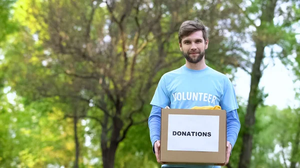 Przystojny Mężczyzna Wolontariusz Gospodarstwo Darowizny Pudełko Ubraniami Stojący Zewnątrz — Zdjęcie stockowe