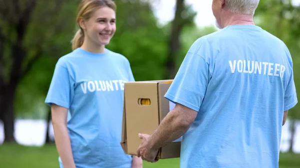 Sorrindo Jovem Mulher Dando Caixa Doação Para Voluntário Sênior Projeto — Fotografia de Stock