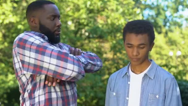 Strict black dad looking at guilty teenage son, upbringing methods, family — ストック動画